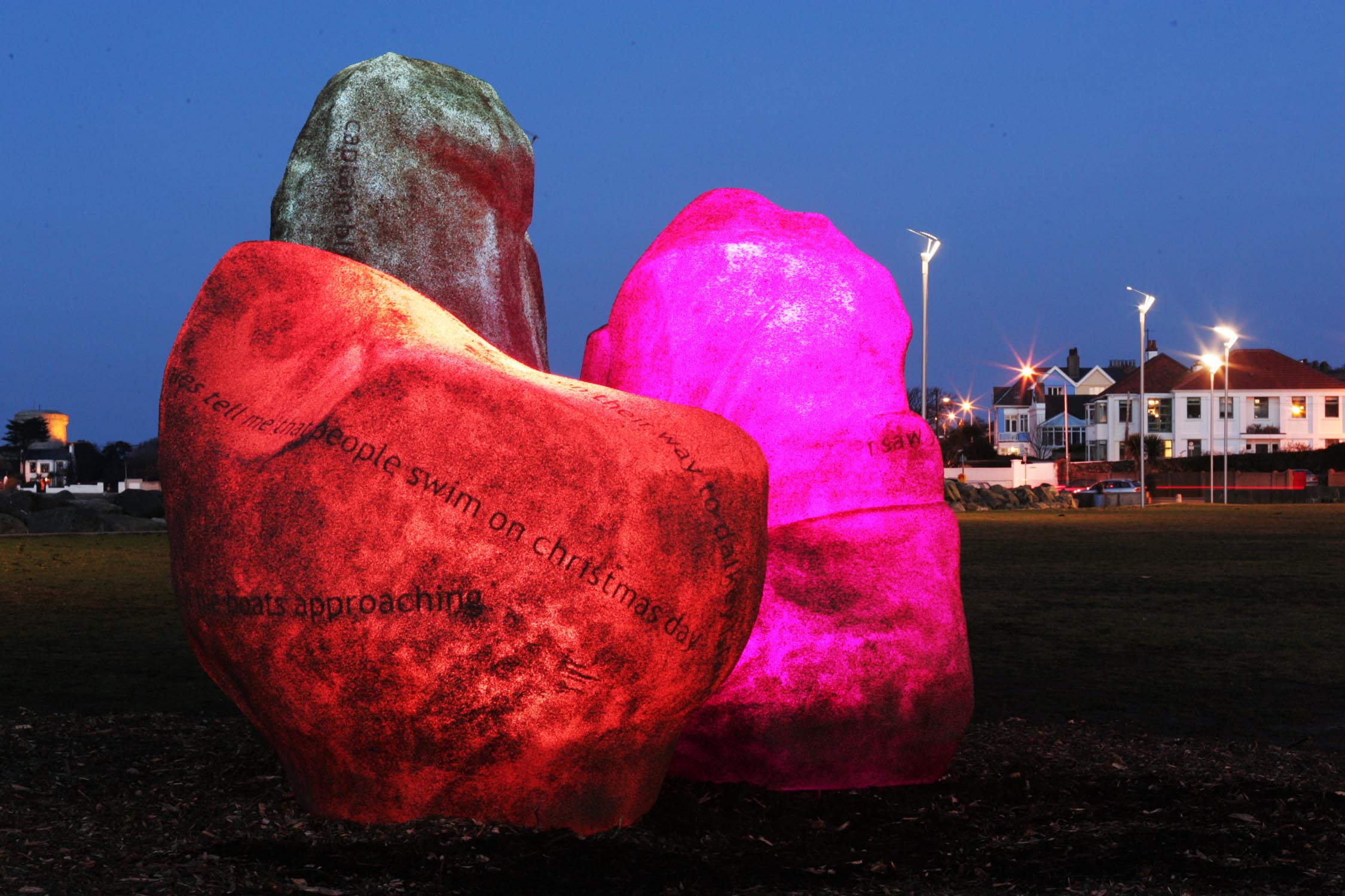 3 boulders are grouped together in a dark park. The boulders are glowing a range of pink colours