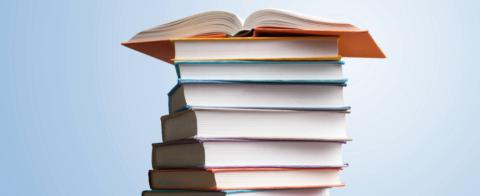 A stack of generic books with a book on top of the stack open