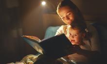 Parent reading a book with a young child by lamp light